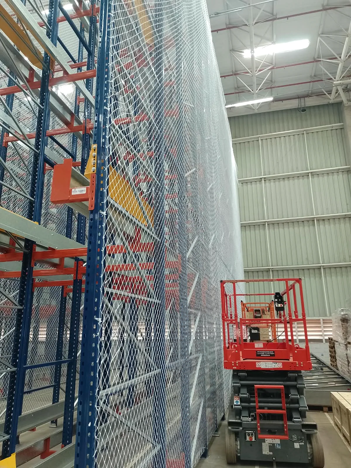 Plataforma elevatória elétrica posicionada junto aos afastadores estruturais de porta-paletes com rede CARRÊ