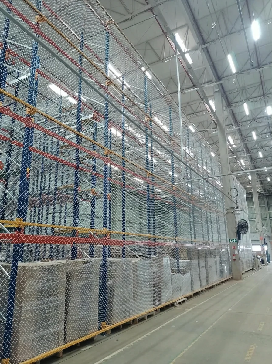 Linha extensa de porta-paletes contendo paletes strechados protegidos por rede de proteção antiqueda CARRÊ