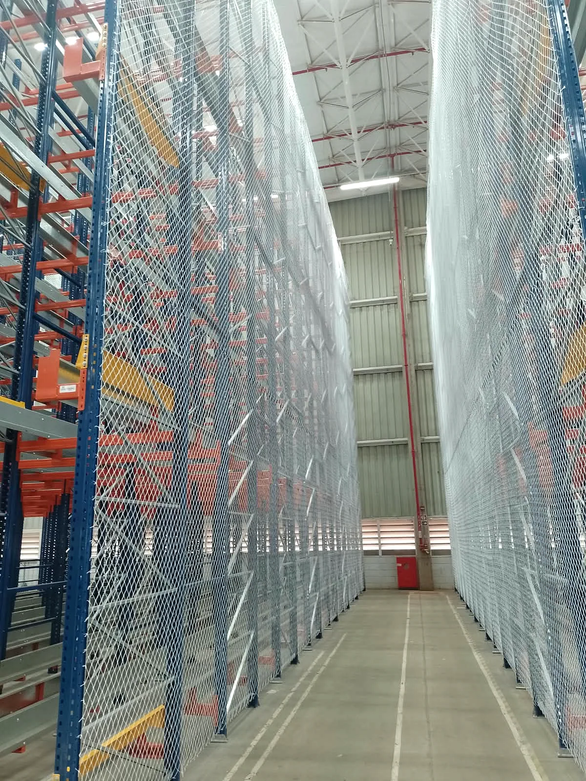 Vista interna de corredor estreito entre duas fileiras de porta-paletes protegidas por rede CARRÊ