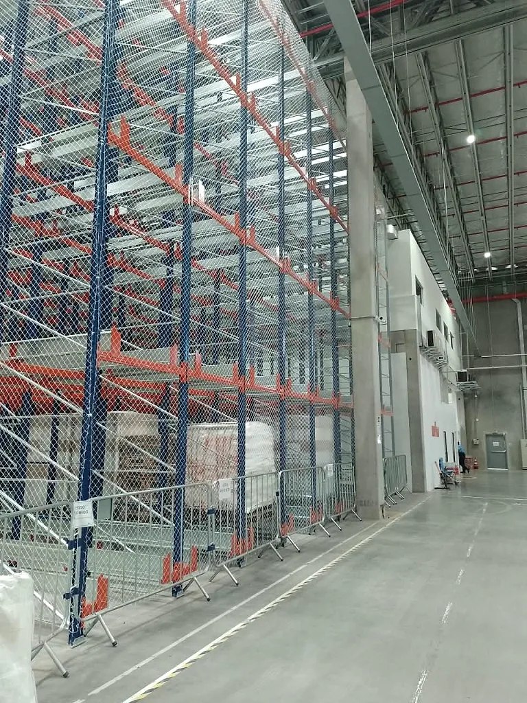 Porta-paletes de alta elevação com rede de proteção CARRÊ instalada do piso ao topo, ao lado do corredor de circulação de pessoas e da área de apoio do centro de distribuição