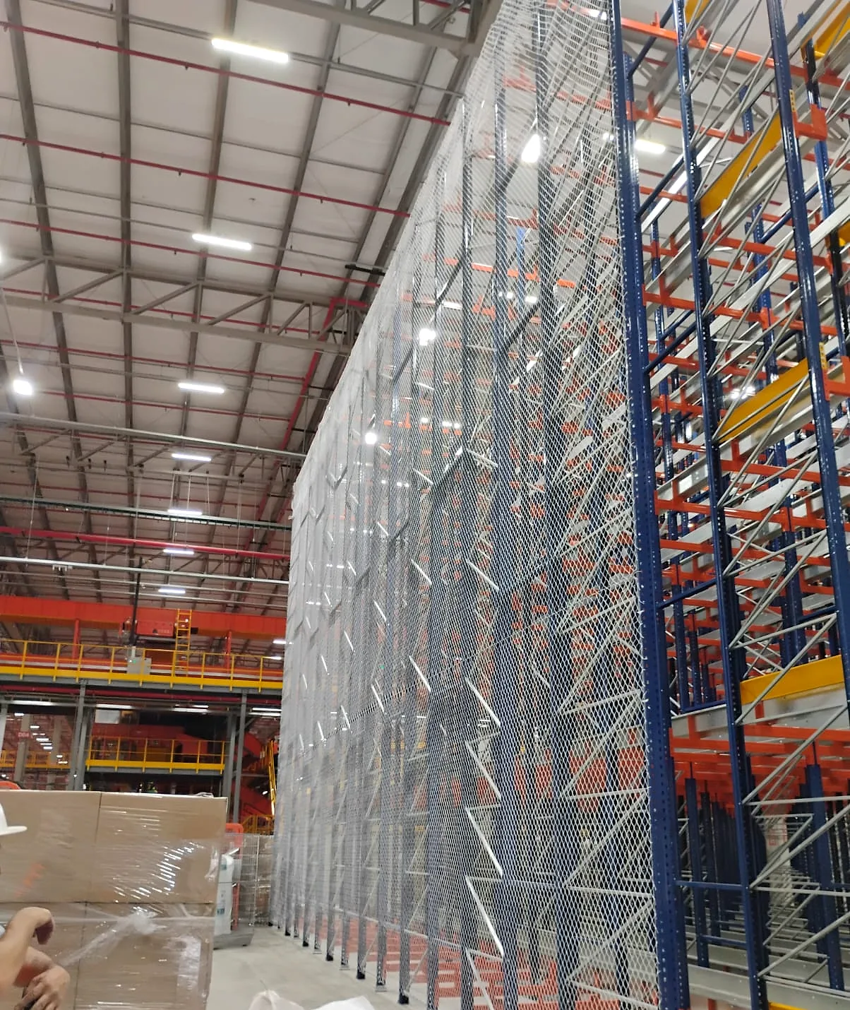 Face lateral inteira de porta-paletes de grande altura fechada com rede de proteção branca CARRÊ do piso até a cobertura do galpão