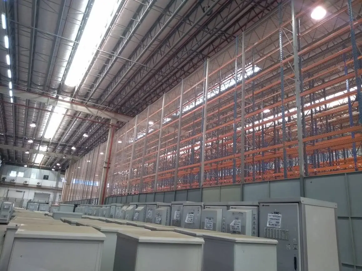 Fechamento vertical de porta-paletes em galpão industrial protegendo equipamentos e área técnica no piso térreo